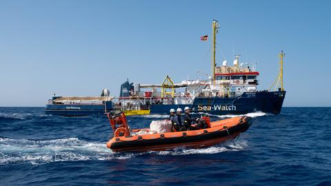 Oranges Rettungsboot mit drei Insassen vor einem Schiff mit Namen Seawatch