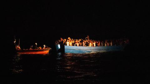 Nachtaufnahme: Ein oranges Rettungsboot neben einem Boot voller Menschen