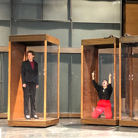 Zwei Schauspielerinnen auf der Bühne in Glaskästen.