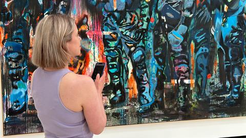 Eine Frau steht vor einem großformatigen Kunstwerk, das Smartphone in der Hand