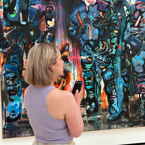 Eine Frau steht vor einem großformatigen Kunstwerk, das Smartphone in der Hand