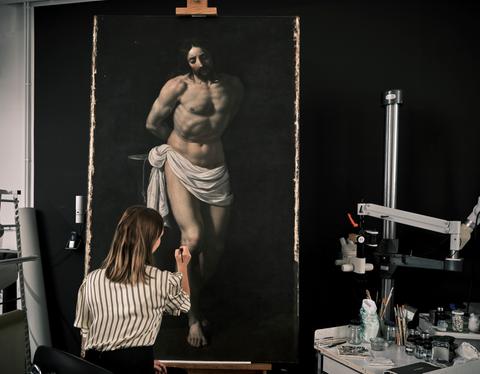Eine Frau arbeitet in einer Werkstatt an einem übergroßen Ölgemälde mit Christus-Motiv