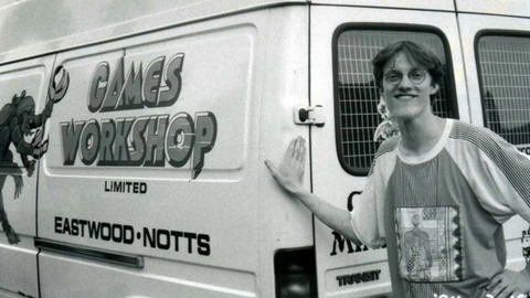 Das Bild zeigt einen jungen Mann mit Brille. Er lehnt an einem Transporter mit der Aufschrift "Games Workshop".