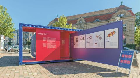 Eine Ausstellungswand mit rotem Hintergrund steht vor einem Gebäude