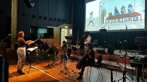 Orchester mit Dirigentin vor einer Leinwand, auf der ein Zeichentrickfilm läuft.