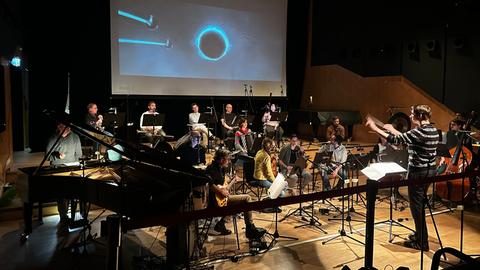 Orchester mit Dirigent vor einer Leinwand, auf der ein Trickfilm läuft.