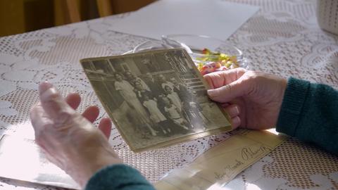 Alte Hände halten eine schwarz/weiß-Fotografie, auf der eine Familie abgebildet ist.