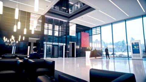 Filmstill des Drehortes "Delphi Invest". Ein Mann geht durch ein großräumliches, modernes Foyer einer Firma.