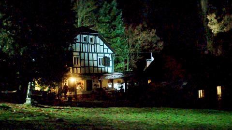 Filmstill des Drehortes "Haus Eva". Ein Fachwerkhaus in einem großen Garten im Dunkeln. 