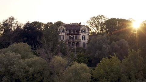 Filmstill des Drehortes "Villa". Eine historische Villa aus der fernen Vogelperspektive fotografiert, umgeben von vielen alten Bäumen.