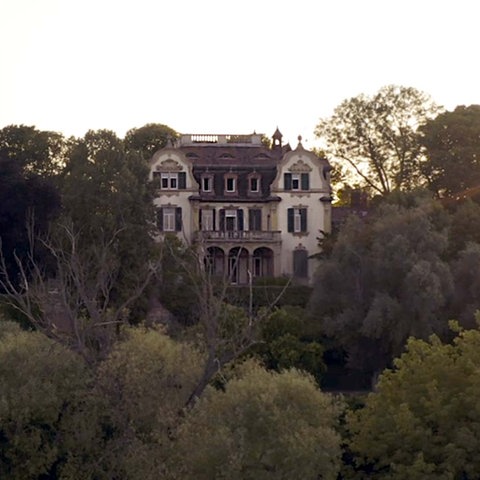 Filmstill des Drehortes "Villa". Eine historische Villa aus der fernen Vogelperspektive fotografiert, umgeben von vielen alten Bäumen.