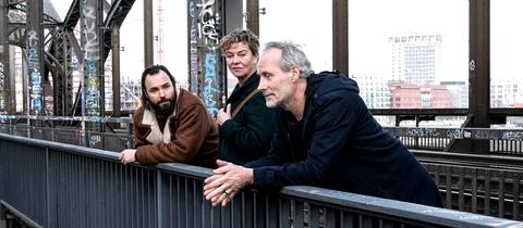 Szene aus Tatort "Luna frisst oder stirbt": Eine Frau und zwei Männer stehen auf einer Brücke und unterhalten sich.