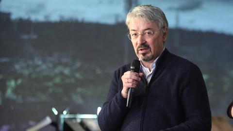 Ein Mann mit blauem Pulli hält ein Mikrofon in der Hand