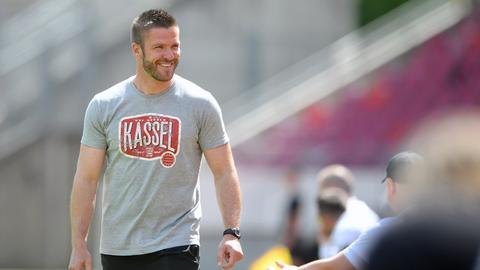 Tobias Damm, Trainer vom KSV Hessen Kassel steht auf dem Spielfeld und trägt ein graues T-Shirt mit rotem Print. Darauf ist "Kassel" zu lesen.