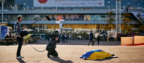 Performance der ukrainischen Künstlerin Maria Kulikovska - eingewickelt in eine Ukraine-Flagge liegt sie auf der Freifläche vor der Halle 3 der Frankfurter Buchmesse