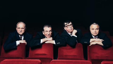 Ulrich Tukur & Die Rhythmus Boys: vier Männer in Anzügen hinter roten Sitzen