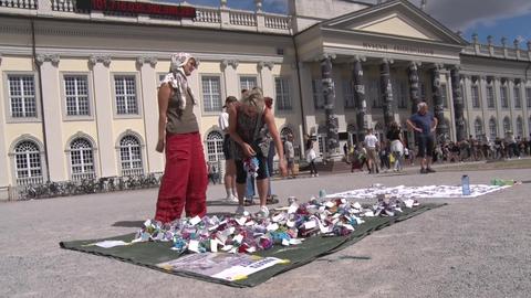 Aktion "Violets against Violence" vor dem Fridericianum - gehäkelte Blumen mit daran befestigten QR-Codes liegen in großer Menge auf einer Decke auf dem Boden - davor mehrere Frauen. 