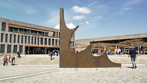Städtischer Platz mit großen Gebäuden im Hintergrund und einer großen Skulptur im Vordergrund