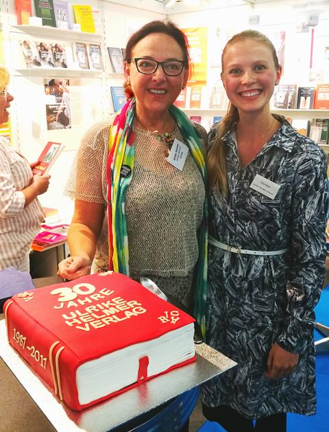 Zwei Frauen an einem Messestand, im Vorgrund eine rote Torte