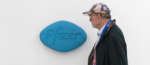 Ein Mann geht an einer übergroßen Viagra-Pille vorbei, die an der Wand hängt.