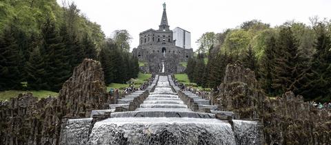 Besucher stehen bei den Wasserspielen im UNESCO-Welterbe Bergpark Wilhelmshöhe an den Kaskaden unterhalb des Herkules-Denkmals.