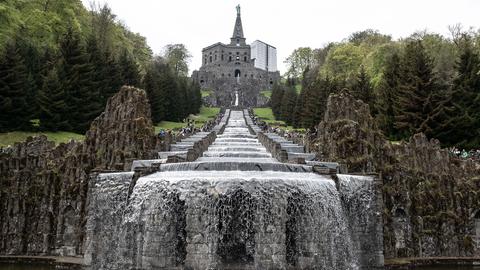 Besucher stehen bei den Wasserspielen im UNESCO-Welterbe Bergpark Wilhelmshöhe an den Kaskaden unterhalb des Herkules-Denkmals.