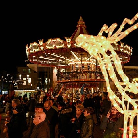 Weihnachtsmarktszene: Beleuchtetes Karussell, Besucher, im Vordergrund eine beleuchtete Rentier-Skulptur.
