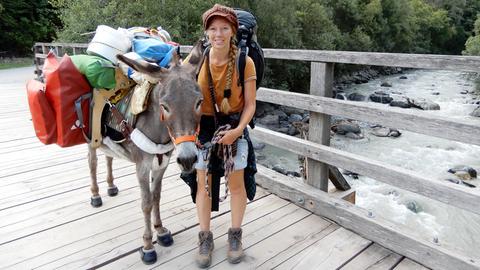 Frau mit Esel und viel Gepäck auf einer Brücke.