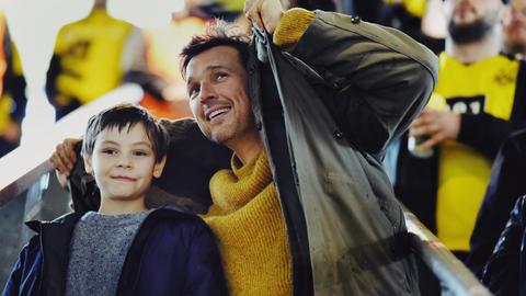 Vater und Sohn im Stadion, der Vater schirmt sie mit seiner Jacke ab.