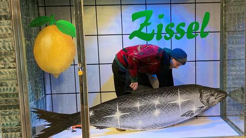 Ein Mann im roten Pulli platziert eine Fisch-Figur in einer Vitrine