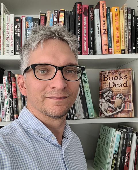 Mann vor einem Bücherregal, darin ein Buch mit Zombie-Cover