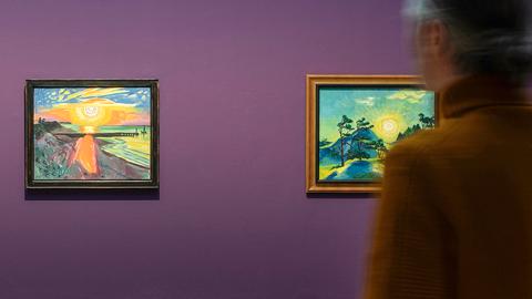 Ein Mensch steht vor zwei gerahmten Gemälden auf einer lilafarbenen Wand