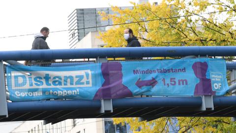 Ein Banner mit der Aufschrift "Distanz! Corona stoppen" hängt an einer Fußgängerbrücke in Offenbach