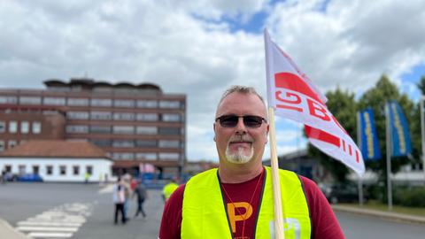Ein Demonstrant der GEW steht mit einer Fahne über der Schulter vor dem Goodyear Fabrikgebäude in Fulda