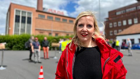 Eine blonde Frau mit roter Jacke steht vor dem Goodyear Fabrikgebäude in Fulda