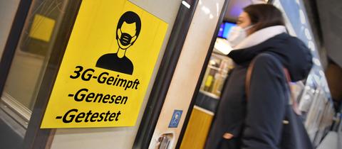 Frau mit Maske steigt in eine Bahn, an deren Tür ein großes gelbes Schild mit "3G-geimpft, getestet, genesen" klebt.