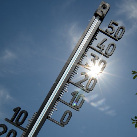 Vor einem strahlend blauen Himmel mit gleißendem Sonnenlicht ist ein Thermometer zu sehen.