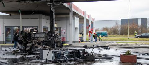 Unter dem Dach einer Tankstelle liegt das Wrack eines ausgebrannten Autos, daneben liegt eine Tankstellen-Säule