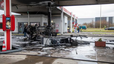 Unter dem Dach einer Tankstelle liegt das Wrack eines ausgebrannten Autos, daneben liegt eine Tankstellen-Säule