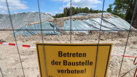 Baustelle mit Erdhügeln, die mit Plastikplane abgedeckt sind. Davor ein Schild "Betreten der Baustelle verboten" an einem Zaun.