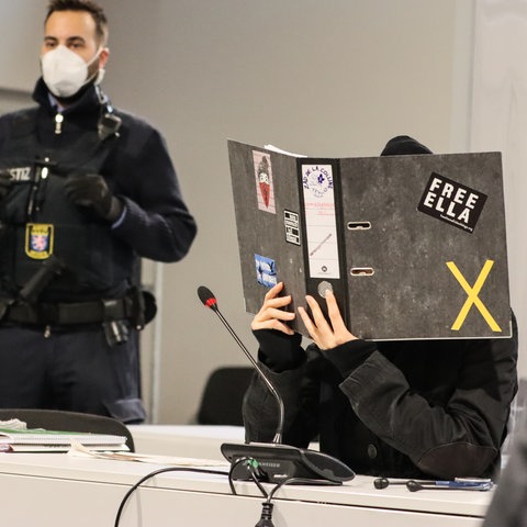 Die weiterhin namenlose Angeklagte im A49-Prozess versteckt ihr Gesicht hinter einem Aktenordner.