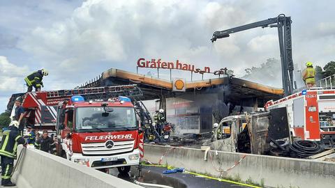 Feuerwehrmänner und -frauen, Feuerwehrautos, ein Lösch-Kran umrahmen die abgebrandte und in Schutt liegende Raststätte Gräfenhausen Ost.
