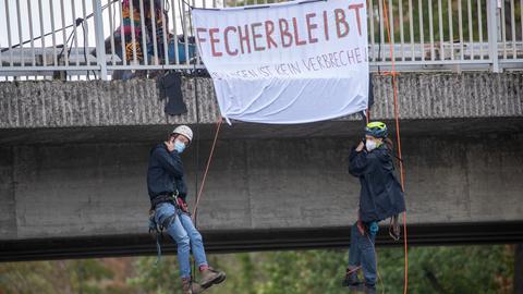 Ein/e Aktivist/in hängt an Seil an Autobahnbrücke