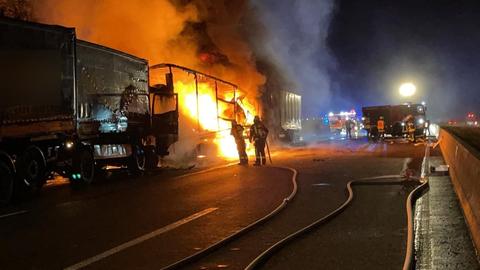 Zwei Feuerwehrleute stehen vor einem brennenden Lkw-Gerippe