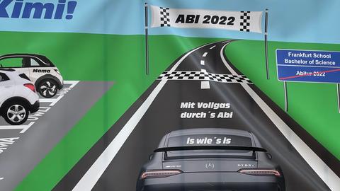 Auf einem Plakat ist ein gezeichneter Sportwagen zu sehen, der auf einer Rennstrecke ins Ziel mit der Aufschrift "Abi 2022" zufährt.