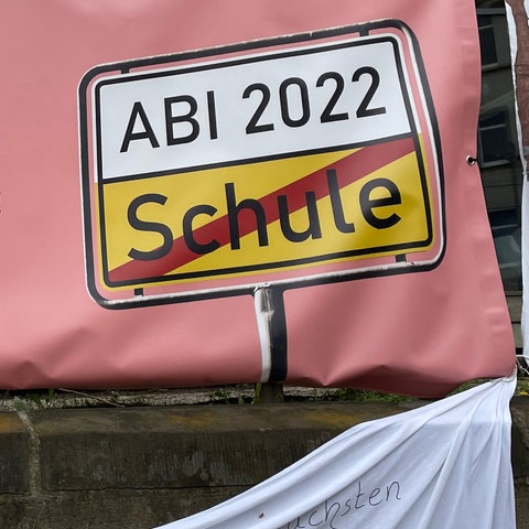 Auf einem rosafarbenen Plakat steht in weißer Schrift "Stella, du schaffst das!" Daneben ein Straßenschild mit der Aufschrift "Abi 2022".