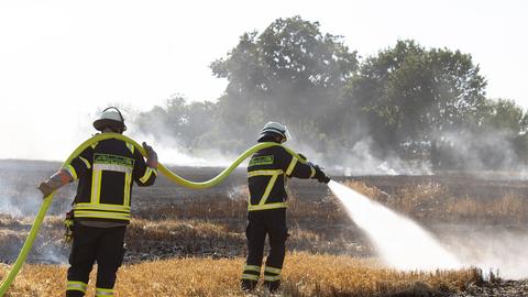 Zwei Feuerwehrmänner bekämpfen einen Brand auf einem abgemähten Acker.