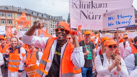 Eine Gruppe von Menschen in orangen Warnwesten und mit weißen Arztkitteln demonstriert auf einem Rathausplatz.