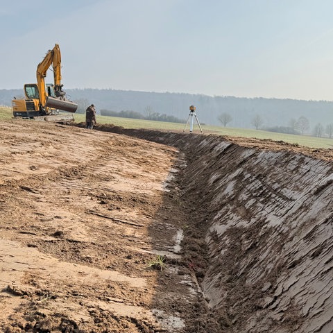 Żółty koparka na polu. Rowy można zobaczyć na pierwszym planie.