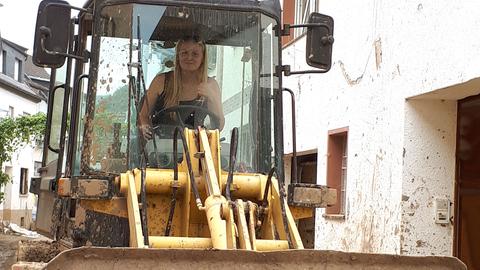 Frau fährt auf einem Bagger durch eine Straße im Ahrtal